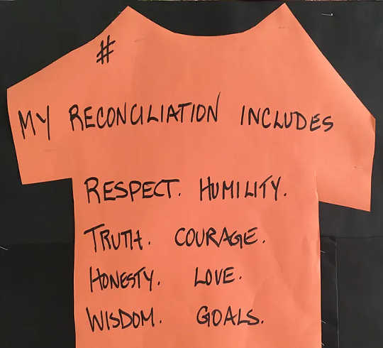 A handmade paper orange T-shirt reads: ‘My reconciliation includes respect, humility, truth, courage, honesty, love, wisdom, goals. (how racism leads to poor attendance in schools)